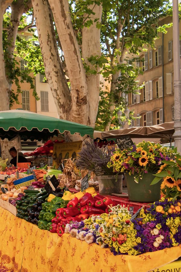 The Place Richelme Market. There are bell peppers, zucchinis, carrots, flowers, and more produce on the yellow tablecloth