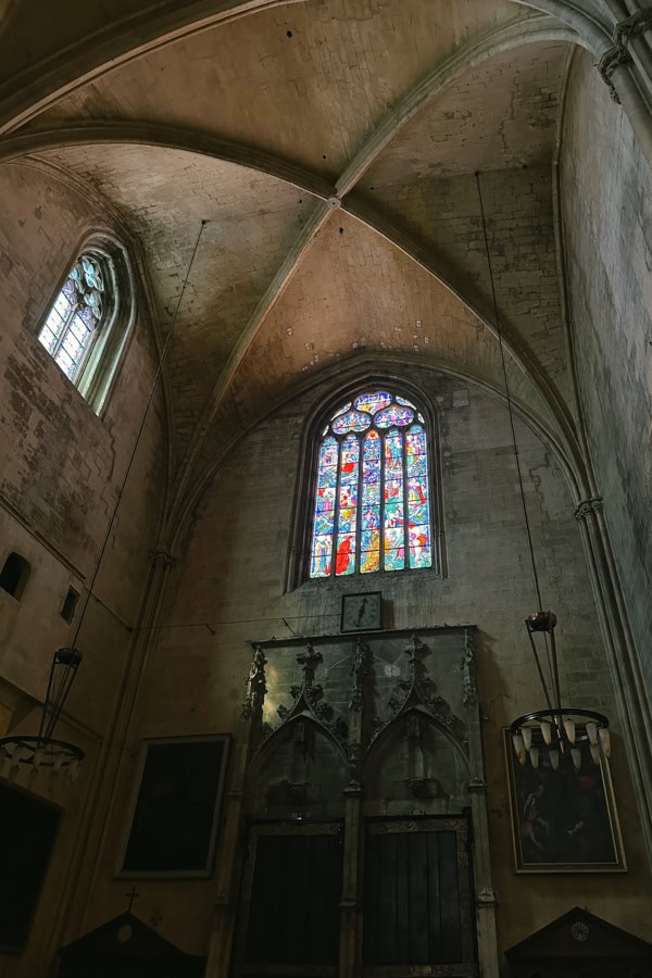 The interior of the Saint-Sauveur Cathedral. There is a large stained glass window towards the top of the arched wall.