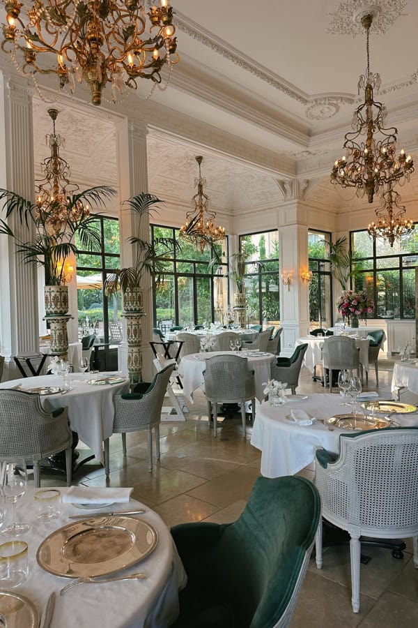 The opulent dining space at Villa Saint-Ange. There are chandeliers hanging from the ceiling, and multiple tables with white tablecloths.