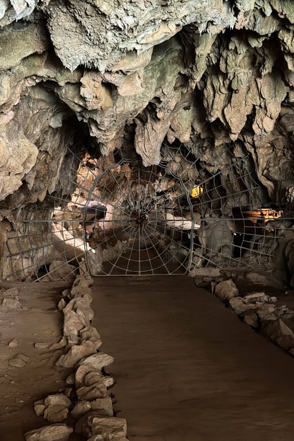A path leading to the entrance to Crystal Cave. There is a metal gate made in the shape of a spider web.